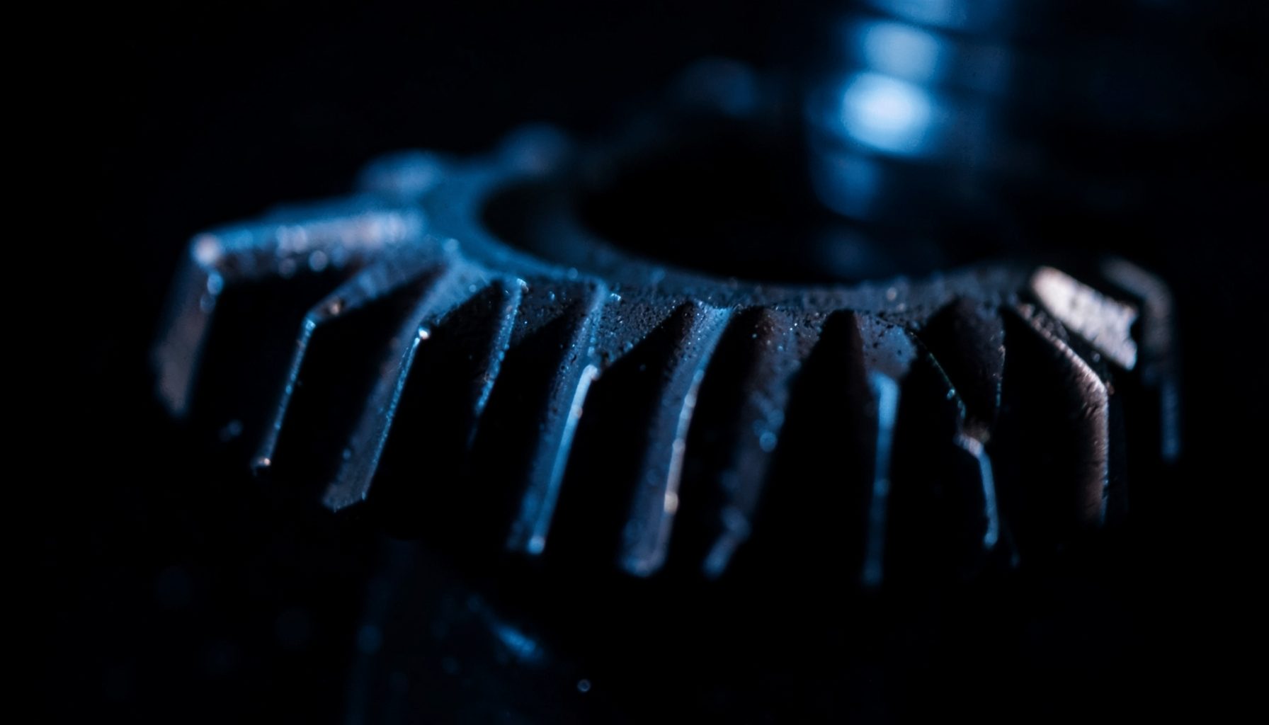 Close-up of precision-machined aerospace gear teeth with a dark metallic finish, set against a deep black background with subtle blue industrial lighting