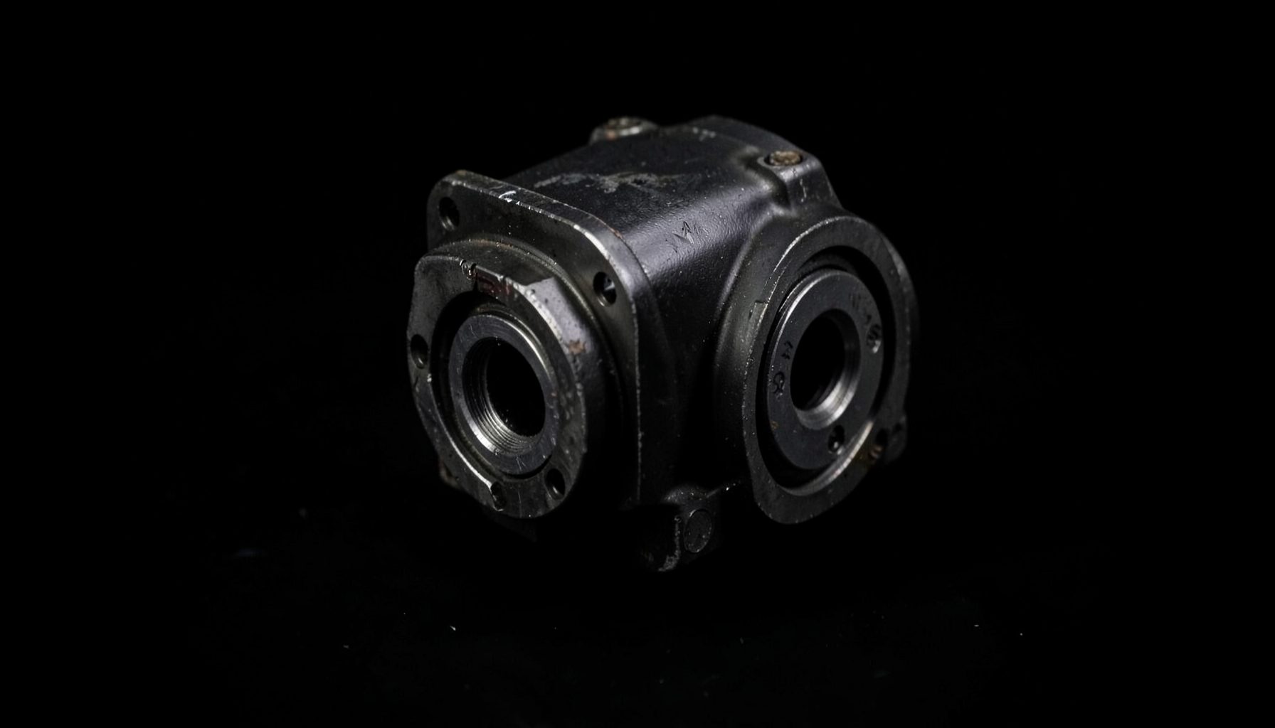 Dark metallic gearbox component on a black background with subtle industrial lighting